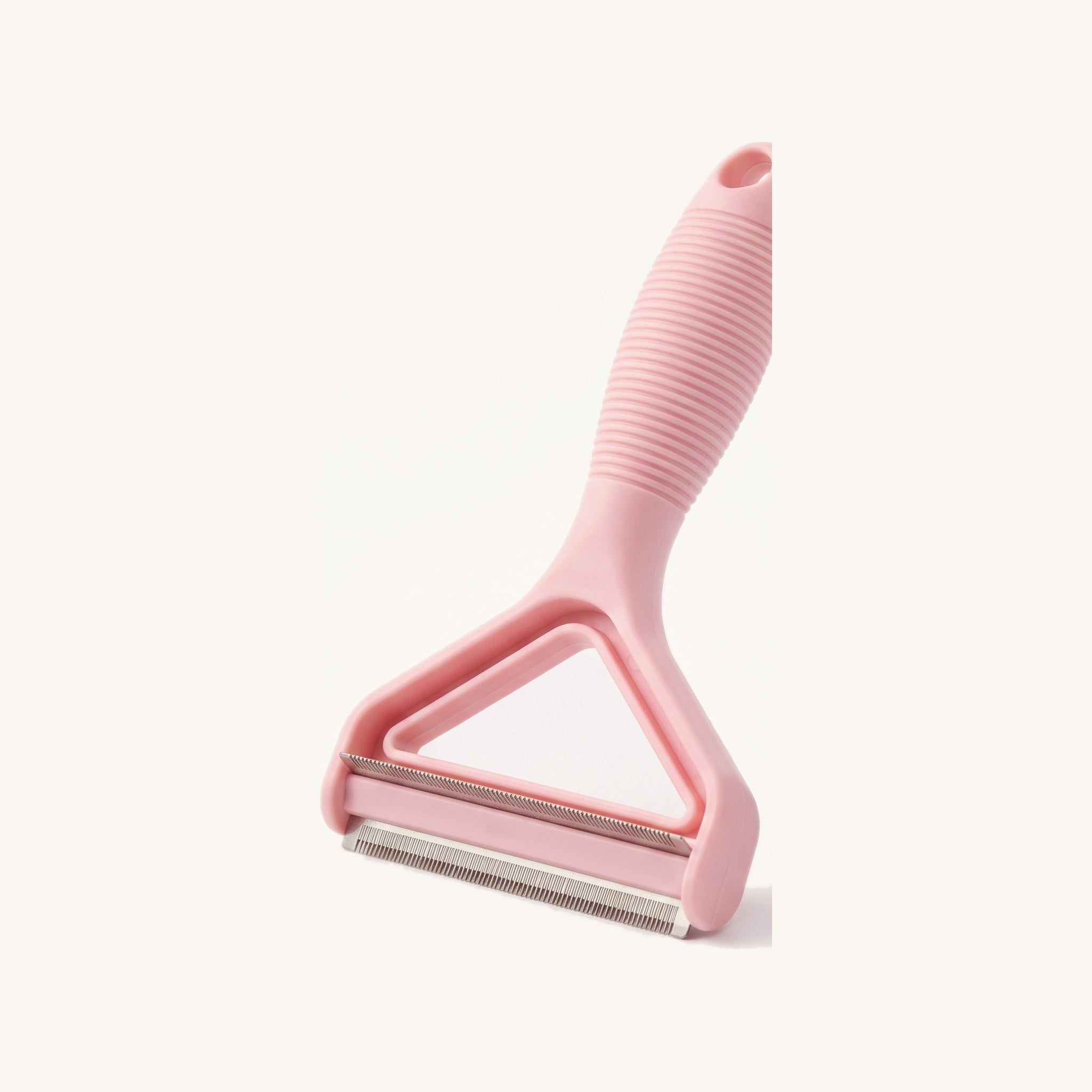 Pink handheld pet hair remover with stainless blade, on a warm off-white background